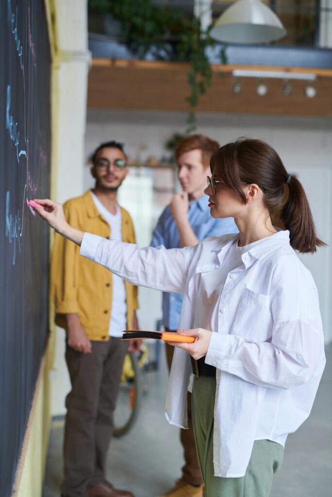 pexels photo 3184644 3184644 A group of young people discussing ideas at a blackboard in a modern office setting.